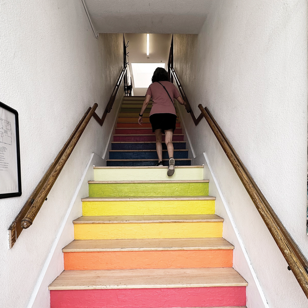 a woman walking up a wide staircase that have been painted bright colors for every step
