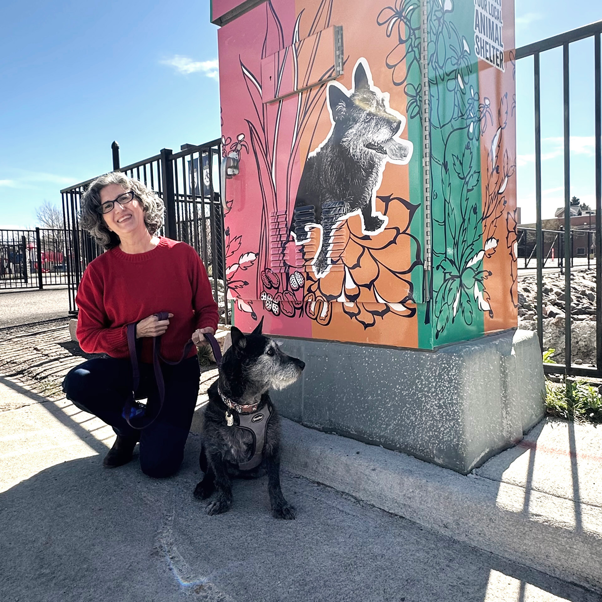 woman and dog in front of an electrical box with a colorful art wrap that includes an image of the same dog